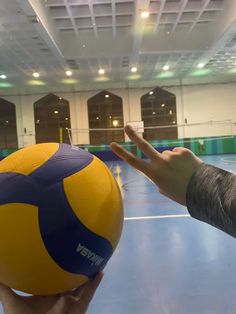 a hand reaching out towards a yellow and blue ball in an indoor gym with lights on the ceiling