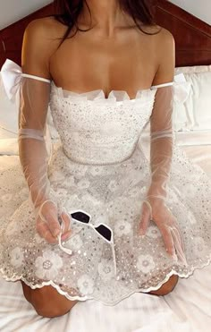 a woman sitting on top of a bed wearing a white dress