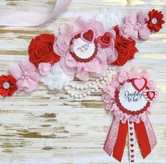 two red and white flowers are next to each other on a wooden surface with pink ribbon