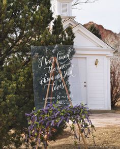 a sign that is sitting in front of a church with purple flowers on the ground