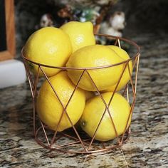 a wire basket filled with lemons sitting on top of a marble counter next to a window