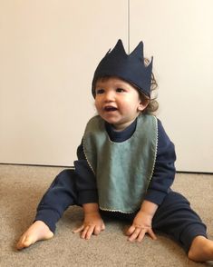 a baby sitting on the floor wearing a bib with a crown on it's head