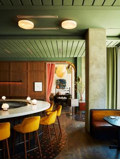 a bar with yellow chairs in a room next to a table and some lights hanging from the ceiling