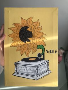 a person holding up a piece of art with a sunflower on it