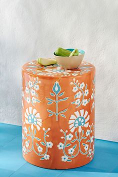 an orange and white painted stool with a bowl on it's top next to a wall