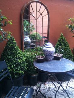 an outdoor table and chairs with potted plants in front of a mirror on the wall