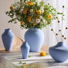 three blue vases with yellow and white flowers in them sitting on a dining room table