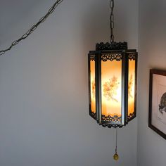 a lamp hanging from the side of a white wall next to a framed picture on a chain