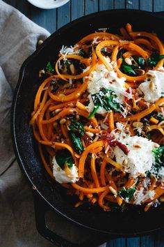 a skillet filled with pasta, cheese and spinach on top of a table