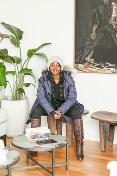 a woman sitting on a chair in front of a table with books and a plant