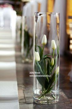 white tulips are in a clear vase on the counter top at a wedding reception