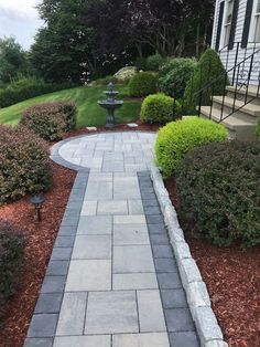 a stone walkway in front of a house with bushes and shrubs on either side of it