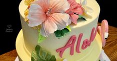 a white cake with pink flowers and the word aloh on top is sitting on a table