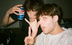 two young men are making the peace sign with their fingers and holding a pepsi can