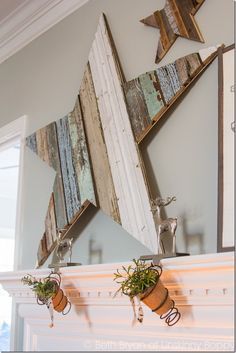 a white fireplace with some potted plants on top of it and two wooden stars above the fire place