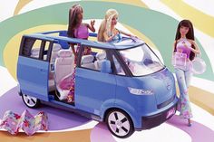 two barbie dolls standing next to a blue minivan