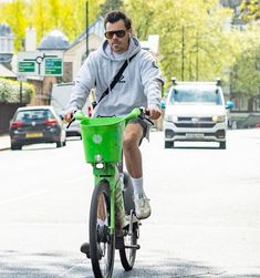 a man riding a bike with a green basket on the front and back wheels, in an urban setting