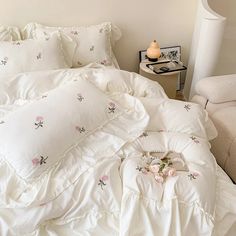 an unmade bed with white sheets and pink flowers on the comforter, next to a night stand