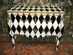 a black and white checkered chest with gold trimmings on the top, sitting in front of a tapestry