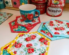 four coasters with flowers on them sitting on a table next to coffee cans and napkins