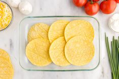 several tortillas in a glass dish next to green onions and tomatoes