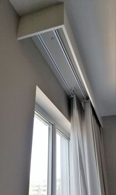 an open window with white curtains in front of it and a curtain rod hanging from the ceiling