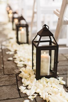 a row of lanterns with white flowers on the ground next to each other and candles in them