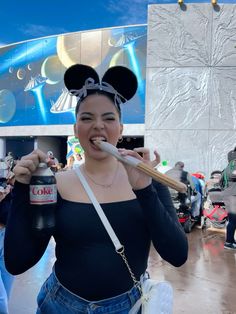 a woman in mickey mouse ears is brushing her teeth with a toothbrush and holding a soda