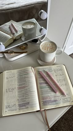 an open book sitting on top of a table next to a coffee cup and pen