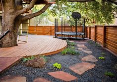 a backyard with a tree, swing set and rock path leading up to the deck