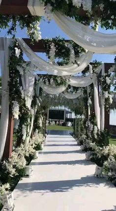 an outdoor wedding ceremony with white flowers and greenery on the side of the aisle