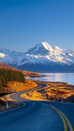 an empty road with snow covered mountains in the background and water on both sides,