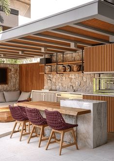 an outdoor kitchen and dining area with stone walls, wood ceilinging and wooden chairs