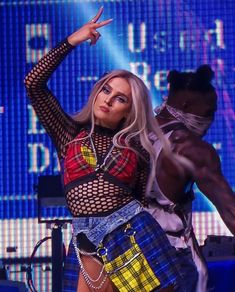 lady in plaid shirt and skirt on stage with arms up to the side as she holds out her right hand