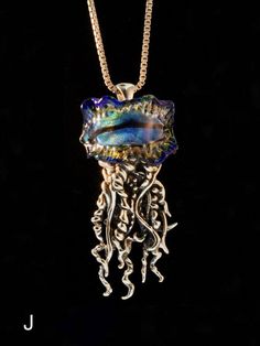 "This dramatic Portuguese Man of War Jelly Fish Pendant wears a crown of dichroic glass. The coiled and flowing tentacles are cast in sterling sliver and the overall length of the pendant is 2-3/8\" (60 mm) long. This is Alisha's second and most complex design collaboration with glass artist John Rizzie who has created a rainbow of dichroic glass crests from which Alisha's coiled sterling silver tentacles descend. Each dichroic glass jelly fish crest is unique so choose from a rainbow of colors. Ocean-inspired Silver Glass Jewelry, Ocean-inspired Silver Glass Necklace, Whimsical Silver Glass Jewelry, Jellyfish Tentacles, Jellyfish Necklace, Magic Charms, Complex Design, Jewelry Ocean, Sea Jewelry