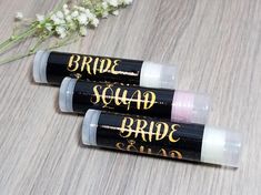 three lip bales with the words bride squad on them sitting next to some flowers