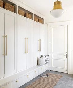 a room with white cupboards and baskets on the floor, along with a rug