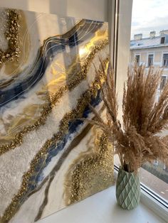 a vase filled with dry grass sitting on top of a window sill next to a painting