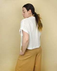 a woman standing in front of a wall with her back turned to the camera, wearing brown pants and a white t - shirt