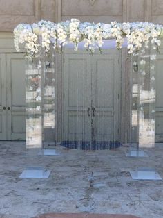 an arrangement of white flowers and greenery in front of a door with glass panels