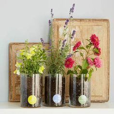 three tin can vases with flowers in them on a shelf next to a wooden frame