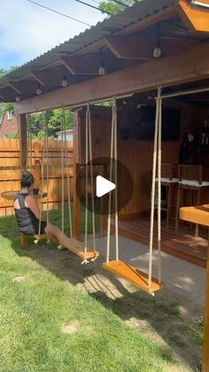 a woman sitting on a swing set in the grass next to a wooden fence and building