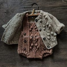 two knitted sweaters are hanging on a wooden surface, one is brown and the other is gray