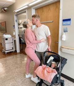 a man and woman are standing next to a baby in a stroller while holding onto each other