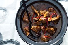 a bowl filled with meat and sauce on top of a table next to utensils