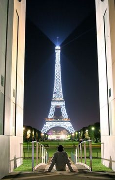 a man sitting in front of the eiffel tower at night