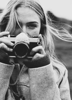 a black and white photo of a woman holding a camera in front of her face