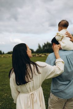 a man holding a baby up to his face while standing next to a woman in a field