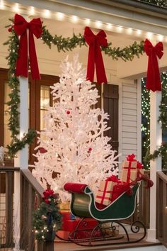 a white christmas tree sitting on top of a porch next to a sleigh