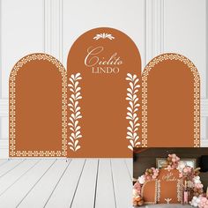 an orange and white photo booth with flowers on the floor next to two archways